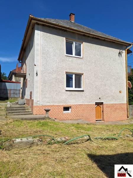 A family house in Šíd with a steep roof and a landscaped garden with a lawn.