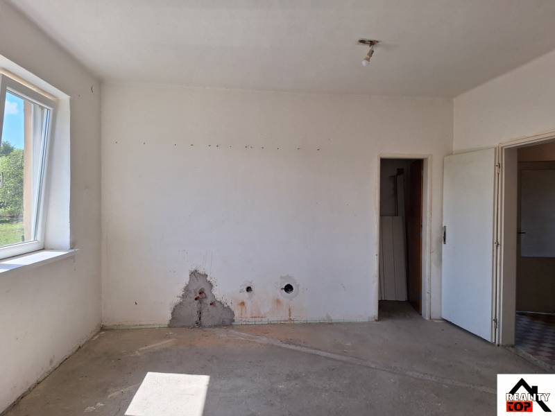 An empty room in a family house with a window and a damaged wall.