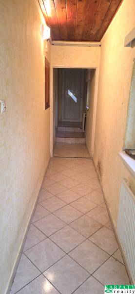 A narrow interior hallway with tiles and a wooden ceiling in a family house.