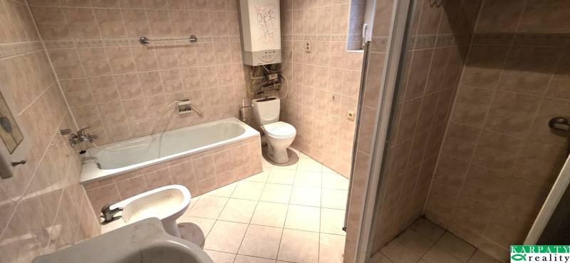 Bathroom in a family house with a bathtub, sink, and toilet. Light-colored tiles.