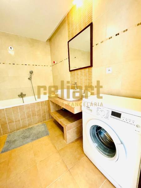 Bathroom with a bathtub and a washing machine in a 4-room apartment, floor with wood decor.