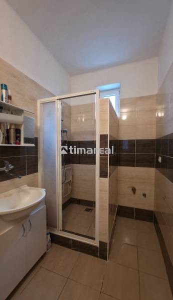 A bathroom with a sink and a shower, decorated in light-toned tiles.