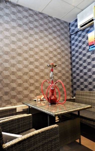 In the commercial space, you can see rattan furniture, a glass table, and a hookah on a geometric wallpaper.