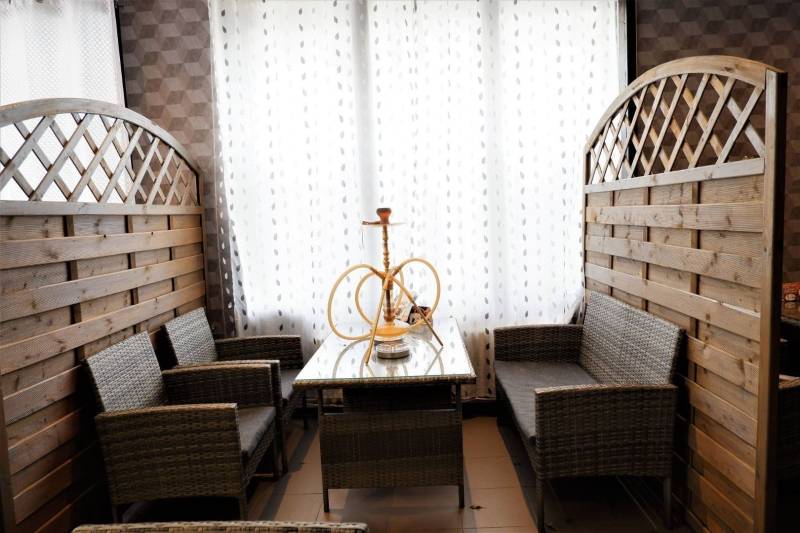 Rattan seating with a hookah, white curtains, and wooden panels in commercial spaces.