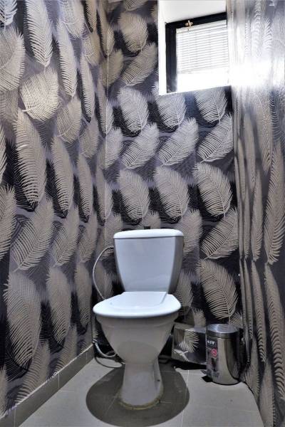 A toilet with decorative wallpaper featuring a leaf pattern and a small window above.