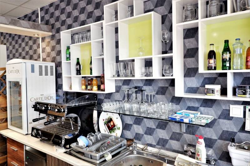 Interior of commercial space with a coffee machine, shelves, glasses, and drinks on the shelves.