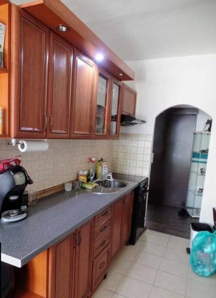 A kitchen in a 3-room apartment with wooden cabinets and a tiled wall above the countertop.