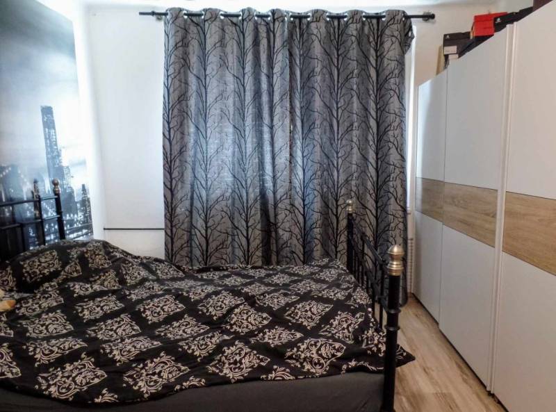 Bedroom in a 3-room apartment with a patterned curtain and a wardrobe, with a wooden decor floor.