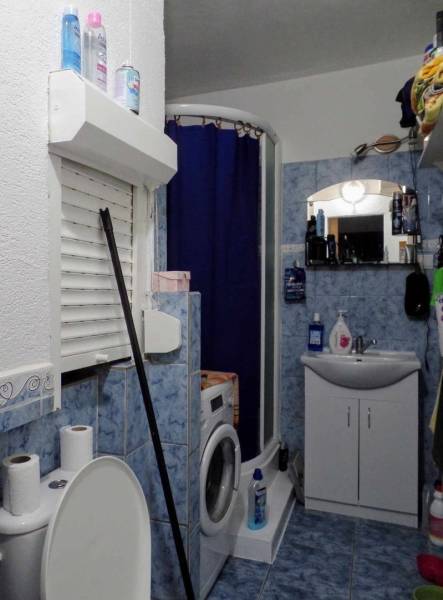 A bathroom in a 3-room apartment with blue tiles, a washing machine, and a shower corner.