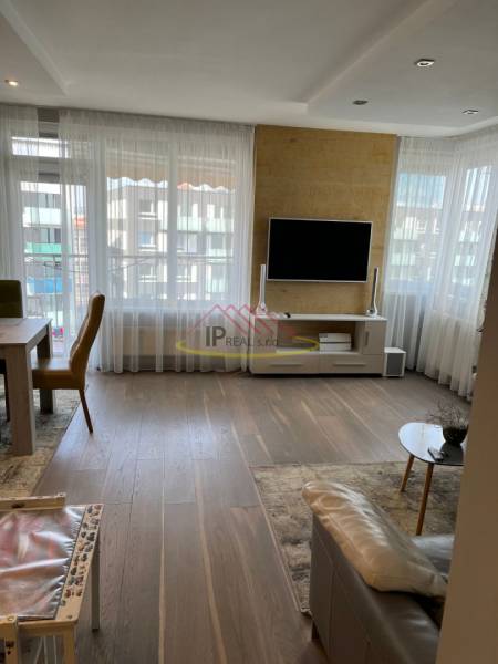 Living room in a four-room apartment with a wooden decor floor and a television on the wall.