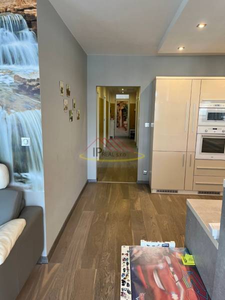 Living room in a 4-room apartment with a wooden decor floor and a kitchen unit.