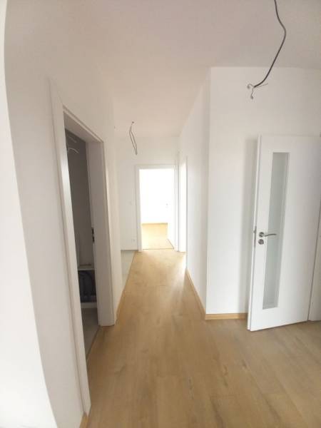 A hallway in a family house with white walls and a wooden-patterned floor.