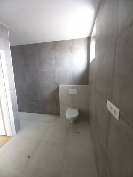 Bathroom in a family house with gray decor tiles and a wall-mounted toilet.