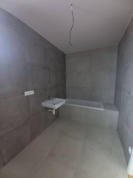 A bathroom with large-format gray tiles, a sink, and a bathtub in a family house.