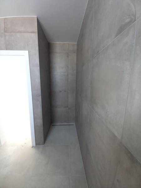 A bathroom in a family house with large-format tiles and a shower area without a tray.