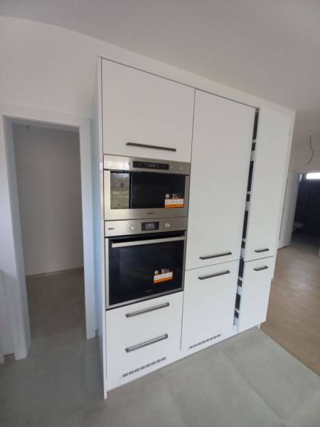 White kitchen unit with integrated appliances in a family house, with a wooden decor floor.