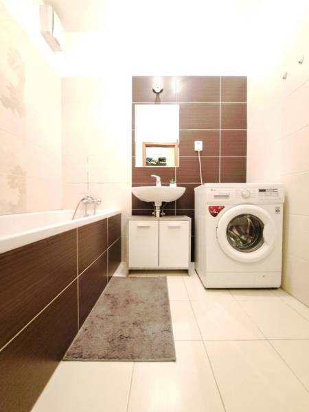 A bathroom in a 2-room apartment with a washing machine, bathtub, and sink.