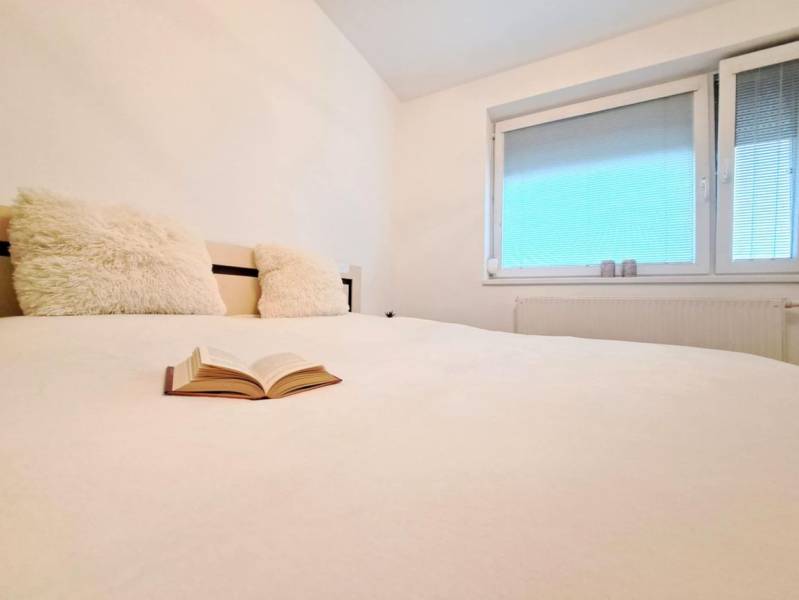 A view of a bed with an open book and a window in a 2-room apartment.