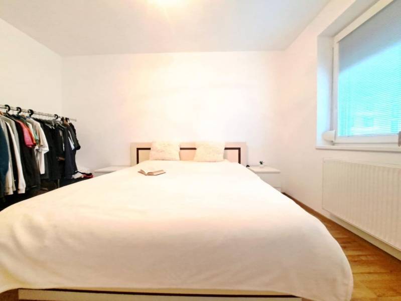 Bedroom in a two-room apartment with a bed, open wardrobe, and wooden decor flooring.