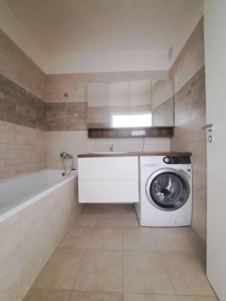 Bathroom in a 2-room apartment with a bathtub, washing machine, and beige tiles.