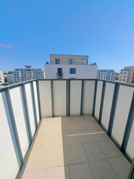 The balcony of a 2-room apartment in Galanta with a view of modern buildings and a blue sky.