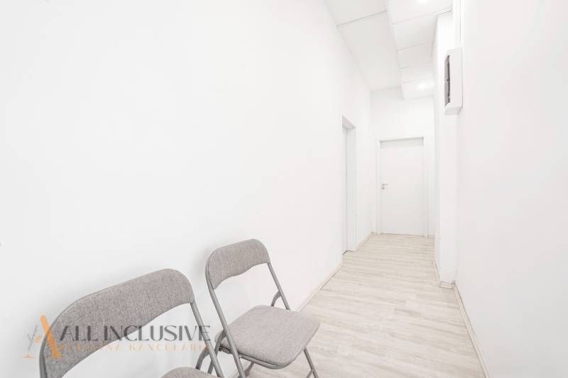 White office walls with two folding chairs, a narrow corridor, and closed doors.