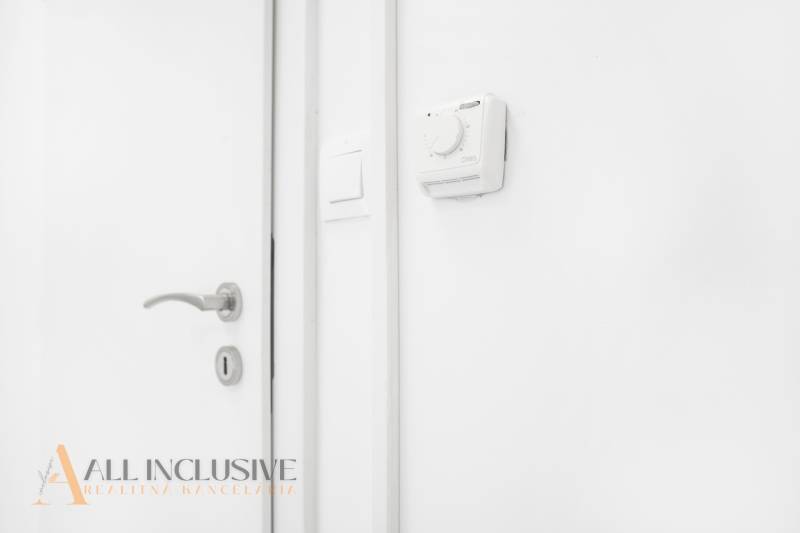 White wall with a thermostat and a handle in the office.