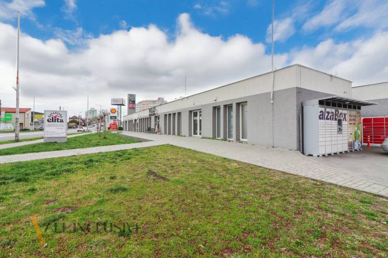 On Vajanského Street, there are commercial spaces, and next to the sidewalk, there is a green lawn.