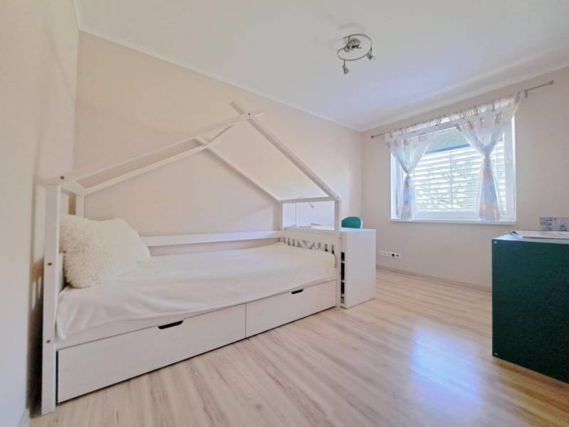 A children's room in a family house with a bed shaped like a house and a floor with a wooden decor.