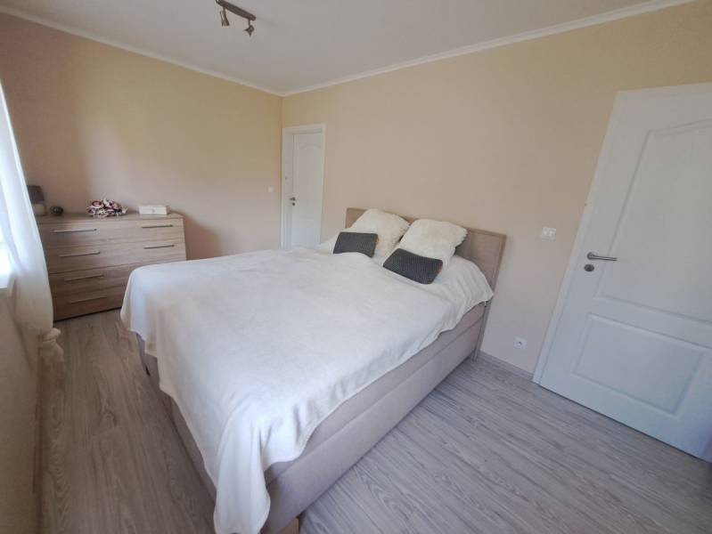 Bedroom in a family house with a bed, dresser, and wooden decor flooring.