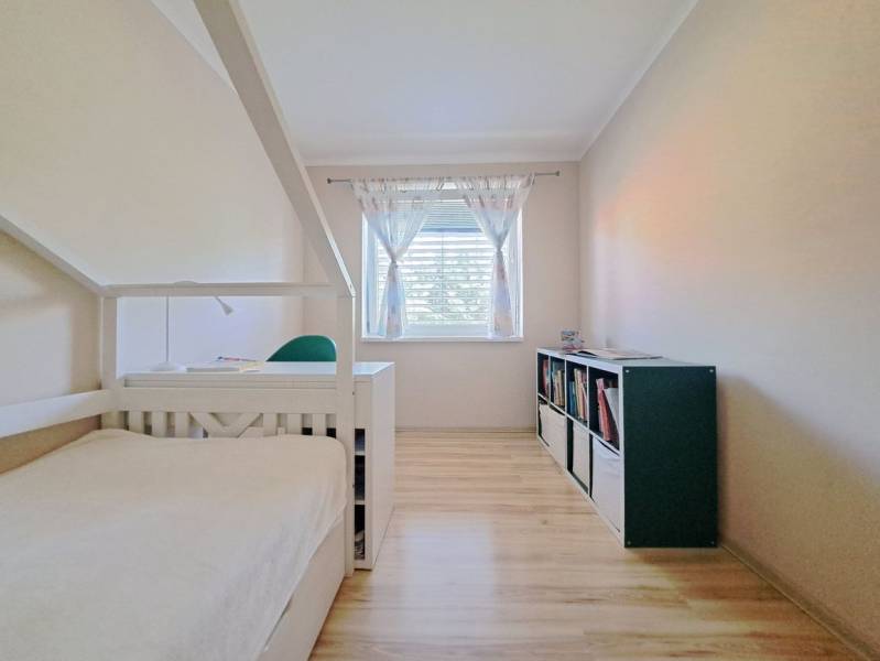 A room in a family house with a bed, a bookshelf, and a wooden-patterned floor.