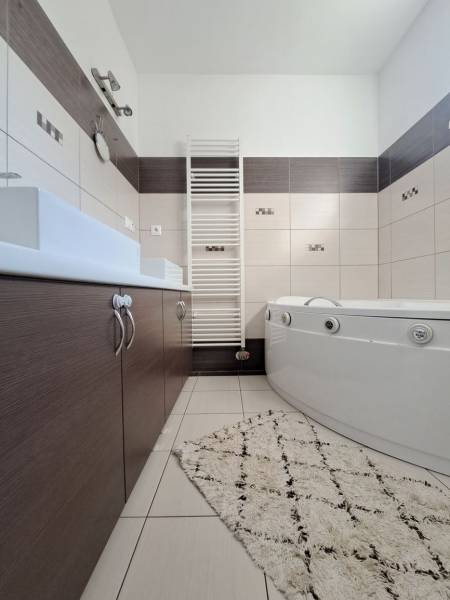 A bathroom in a family house with a bathtub, a sink, a white radiator, and tiles.