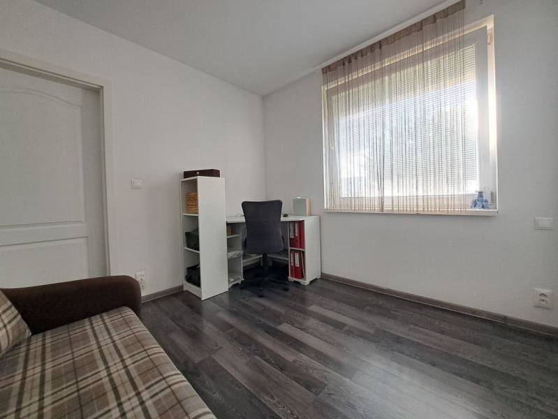 A room in a family house with a wooden decor floor, a table, a chair, and a sofa.
