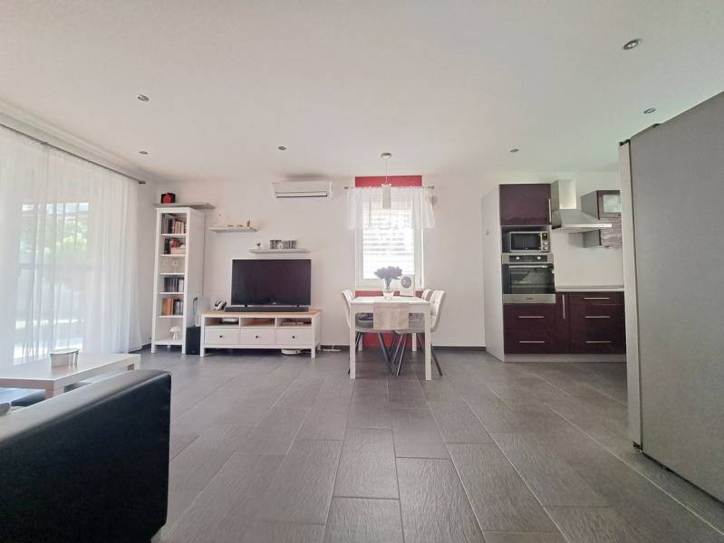 Living room with TV, kitchen, and dining table, floor with wooden decor.