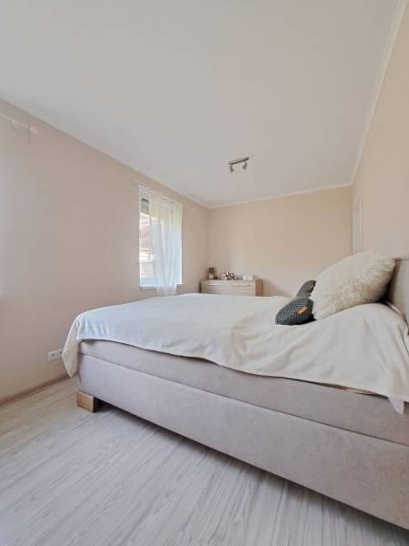 A bright bedroom in a family house with a comfortable bed and a wooden-patterned floor.