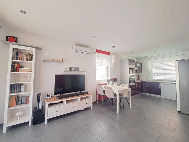 Living room in a family house with a television, kitchenette, and a table with three chairs.