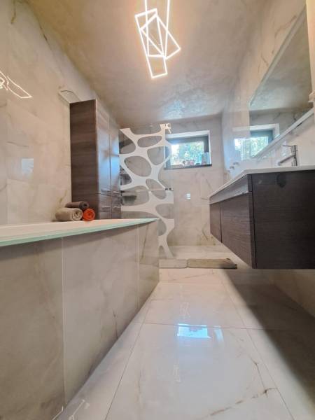 Bathroom in a family house with a bathtub, modern lighting, tiles, and a sink.