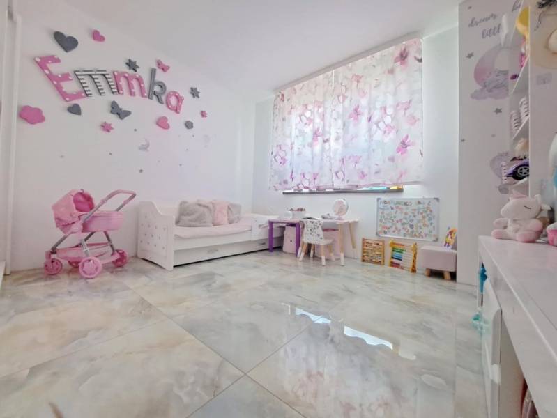 Children's room in a family house with decorations, a stroller, and desks. The floor has a wooden decor.
