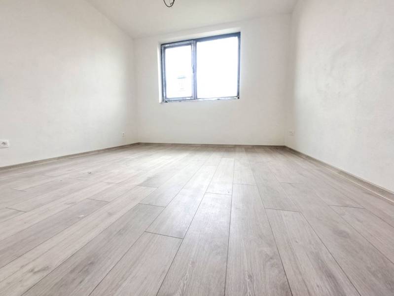 A room in a family house with a wooden decor floor, white walls, one window.