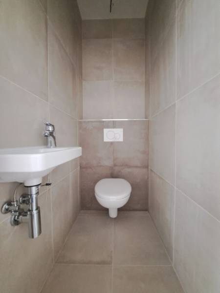 Bathroom in a family house with a toilet and a sink, tiles in neutral shades.