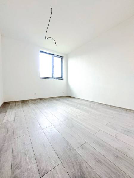 An empty room in a family house with a wood-patterned floor and a window.