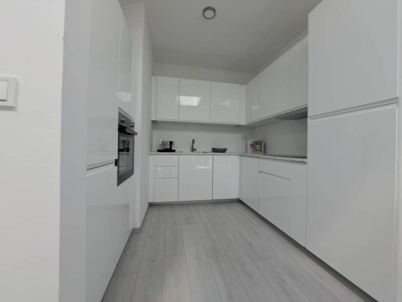 A modern kitchen with white cabinets and a wood-patterned floor in a two-room apartment.