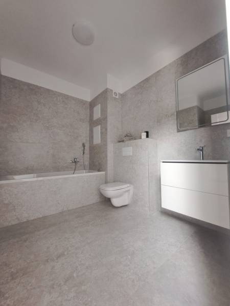 A bathroom with a bathtub, toilet, and sink in a 2-room apartment, the interior has light ceramic tiles.