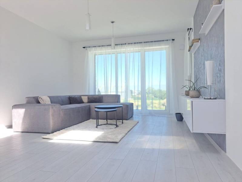 A bright living room in a two-room apartment with large windows and a wooden decor floor.