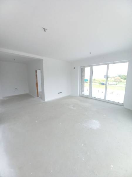 A bright living room in a two-room apartment with large windows and an empty floor.