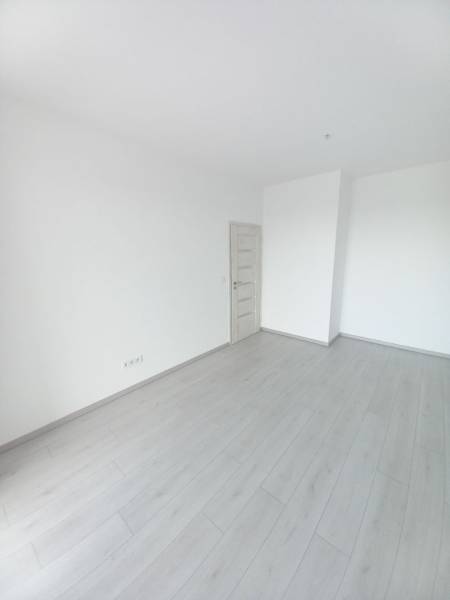 A room in a 2-bedroom apartment with white walls and a wood-patterned floor.