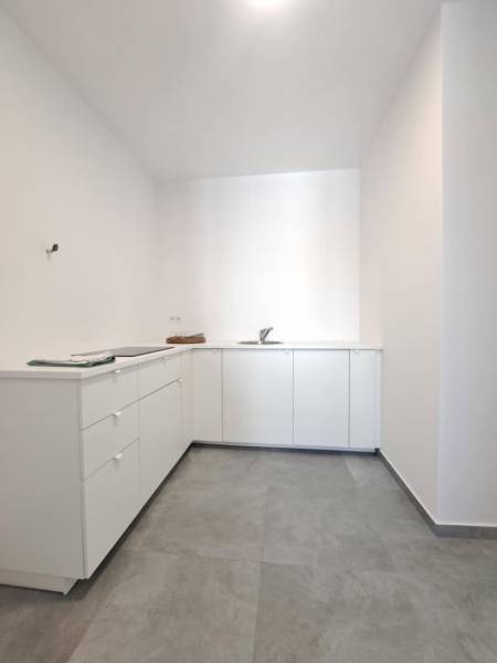 Kitchen area of commercial premises with white furniture and gray flooring.