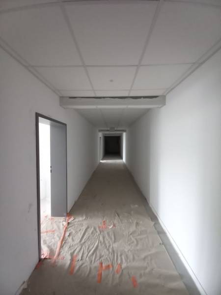 A narrow corridor in commercial premises with white walls and a makeshift floor.