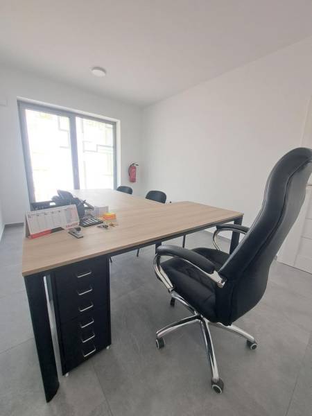 Office with a black chair, a desk with a wood finish, and a window in commercial premises.