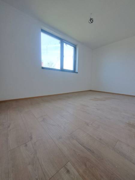 A spacious room with a wood-patterned floor and a large window in a family house.
